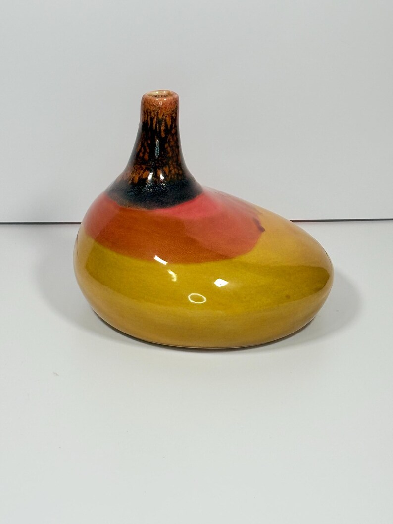 Peut inclure: Un vase en c&eacute;ramique avec un corps arrondi et un col &eacute;troit. Le vase pr&eacute;sente un d&eacute;grad&eacute; de couleurs, passant du jaune &agrave; la base &agrave; l'orange, au rose et au noir en haut. Le vase a une finition brillante.