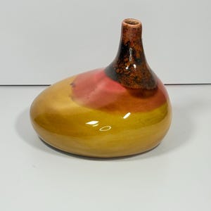 Peut inclure: Un vase en c&eacute;ramique fait &agrave; la main avec une forme organique unique. Le vase pr&eacute;sente un d&eacute;grad&eacute; de couleurs, passant d'une base jaune chaud &agrave; une section m&eacute;diane rose-rouge, et un col brun fonc&eacute;. L'ouverture est de petite forme circulaire.