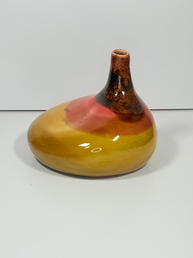 Peut inclure: Un vase en c&eacute;ramique fait &agrave; la main avec une forme organique unique. Le vase pr&eacute;sente un d&eacute;grad&eacute; de couleurs, passant d'une base jaune chaud &agrave; une section m&eacute;diane rose-rouge, et un col brun fonc&eacute;. L'ouverture est de petite forme circulaire.