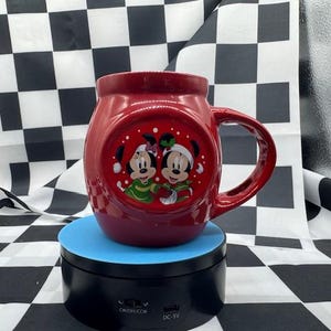 Puede incluir: Una taza de cer&aacute;mica roja con un asa grande, con Mickey y Minnie Mouse con atuendos festivos. La taza tiene un dise&ntilde;o redondo y un acabado brillante. Los personajes est&aacute;n representados en un dise&ntilde;o circular.
