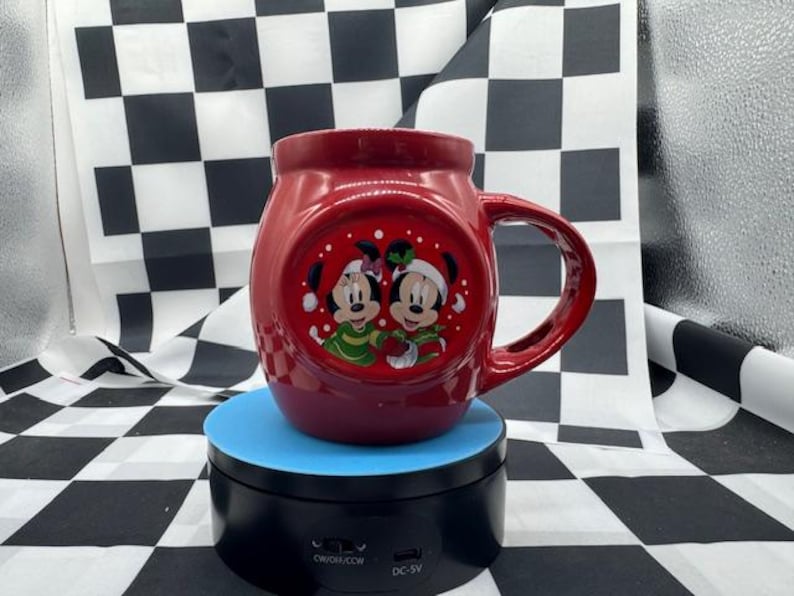 Puede incluir: Una taza de cer&aacute;mica roja con un asa grande, con Mickey y Minnie Mouse con atuendos festivos. La taza tiene un dise&ntilde;o redondo y un acabado brillante. Los personajes est&aacute;n representados en un dise&ntilde;o circular.
