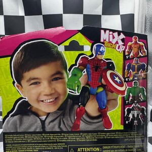 May include: A toy action figure of a superhero, combining elements of Captain America and Spider-Man, holding a shield. The packaging features a smiling child and the text "Mix Them Up". Additional superhero figures are shown on the packaging.