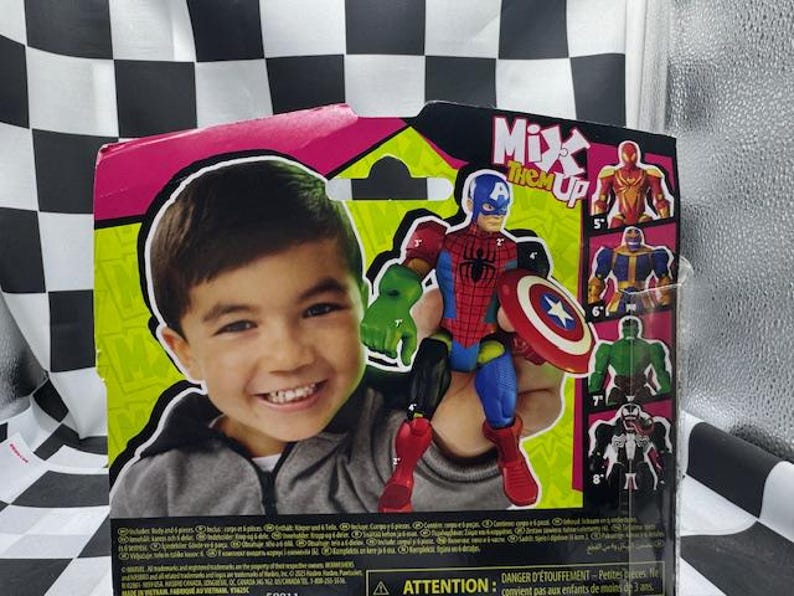 May include: A toy action figure of a superhero, combining elements of Captain America and Spider-Man, holding a shield. The packaging features a smiling child and the text "Mix Them Up". Additional superhero figures are shown on the packaging.