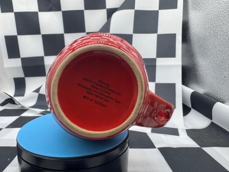 Puede incluir: Una taza de cer&aacute;mica roja con asa, vista desde abajo. La taza tiene un patr&oacute;n texturizado y un interior rojo. La base de la taza tiene texto impreso, incluyendo "&copy;Disney" y "Made in China".