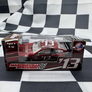 Puede incluir: Un coche de carreras modelo fundido a presión de color rojo con el número 13 en blanco, en un estuche transparente. El embalaje presenta el texto "Martinsville Speedway" y "Ages 4 & up".