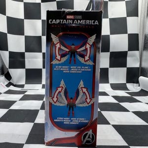 Pode incluir: Uma caixa de figuras de a&ccedil;&atilde;o do Capit&atilde;o Am&eacute;rica da Marvel Studios. A caixa apresenta um gr&aacute;fico do Capit&atilde;o Am&eacute;rica com asas em vermelho, branco e azul. O texto inclui "SLIDE MODE" e "STRIKE MODE" em v&aacute;rios idiomas. O logotipo dos Vingadores &eacute; vis&iacute;vel.