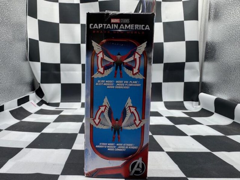 Pode incluir: Uma caixa de figuras de a&ccedil;&atilde;o do Capit&atilde;o Am&eacute;rica da Marvel Studios. A caixa apresenta um gr&aacute;fico do Capit&atilde;o Am&eacute;rica com asas em vermelho, branco e azul. O texto inclui "SLIDE MODE" e "STRIKE MODE" em v&aacute;rios idiomas. O logotipo dos Vingadores &eacute; vis&iacute;vel.