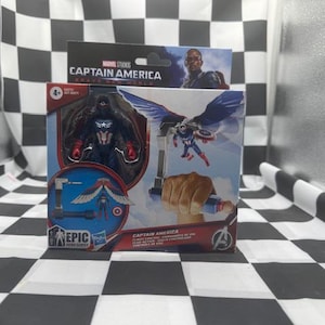 Pode incluir: Um conjunto de figuras de a&ccedil;&atilde;o do Capit&atilde;o Am&eacute;rica numa caixa. A caixa apresenta imagens do Capit&atilde;o Am&eacute;rica em a&ccedil;&atilde;o, com uma figura do Capit&atilde;o Am&eacute;rica com asas. A caixa tamb&eacute;m tem o texto "Captain America Brave New World".
