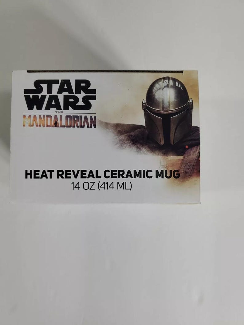 Pode incluir: Uma caixa branca com o logotipo de Star Wars: The Mandalorian e uma representa&ccedil;&atilde;o do capacete do Mandaloriano. A caixa diz "Heat Reveal Ceramic Mug" e tem uma capacidade de 414 ml. O design tem um tema espacial.