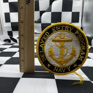 May include: A round Navy patch with gold and blue embroidery. The patch features an anchor design and the words "DELAYED ENTRY PROGRAM NAVY". A wooden ruler is next to the patch, showing measurements in inches.
