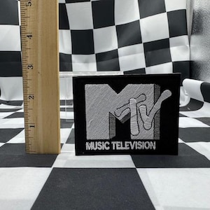 May include: Black patch with the MTV logo in white, with the words "MUSIC TELEVISION" below. The patch is approximately 3 inches wide and 2 inches tall. The background is a black and white checkered pattern.