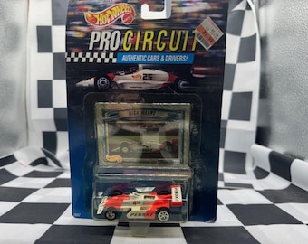 Op de afbeelding: Een Hot Wheels Pro Circuit gegoten raceauto speelgoed in de originele verpakking. De verpakking bevat afbeeldingen van raceauto's en de tekst "Authentic Cars & Drivers!". De speelgoedauto is rood en wit met nummer 4.