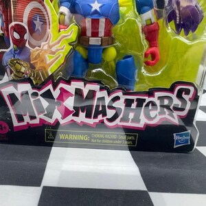 May include: A packaged action figure toy featuring Captain America, Spider-Man, and other characters. The packaging has the text "Mixmashers" in pink and white. The toy is for ages 4+ and has a choking hazard warning.