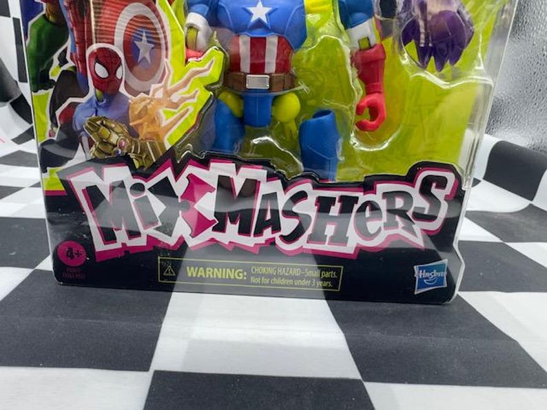 May include: A packaged action figure toy featuring Captain America, Spider-Man, and other characters. The packaging has the text "Mixmashers" in pink and white. The toy is for ages 4+ and has a choking hazard warning.