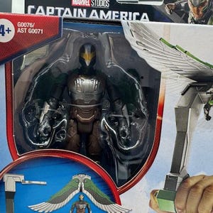 May include: A Captain America action figure featuring the Vulture character. The figure is in a clear plastic package with the Marvel Studios logo. The Vulture figure is black, brown, and silver with green wings. The packaging includes the number 4+.