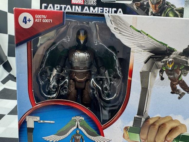 May include: A Captain America action figure featuring the Vulture character. The figure is in a clear plastic package with the Marvel Studios logo. The Vulture figure is black, brown, and silver with green wings. The packaging includes the number 4+.