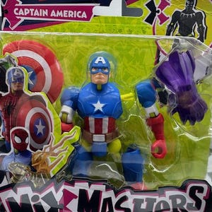 May include: A Captain America action figure in a plastic package. The figure is blue, red, and white, with a star on the chest and a shield. The packaging includes other Marvel characters and the words "Mix Mashers".