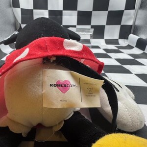 May include: A plush Minnie Mouse doll, featuring a black head and ears, a red and white polka dot skirt, and white gloves. The doll has a tag that reads "KOHL'S cares."