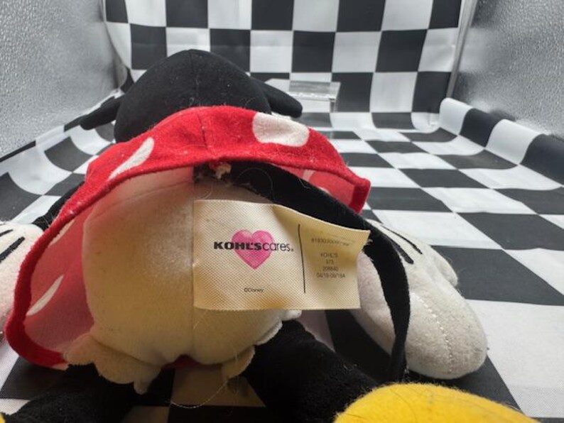 May include: A plush Minnie Mouse doll, featuring a black head and ears, a red and white polka dot skirt, and white gloves. The doll has a tag that reads "KOHL'S cares."