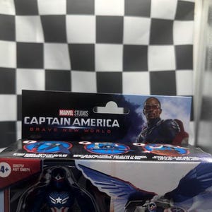 Pode incluir: Uma caixa de boneco de a&ccedil;&atilde;o do Capit&atilde;o Am&eacute;rica da Marvel Studios. A caixa apresenta o texto "Captain America Brave New World" e uma imagem do personagem. O fundo &eacute; um padr&atilde;o xadrez em preto e branco.