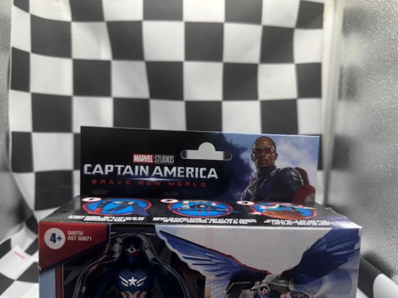 Pode incluir: Uma caixa de boneco de a&ccedil;&atilde;o do Capit&atilde;o Am&eacute;rica da Marvel Studios. A caixa apresenta o texto "Captain America Brave New World" e uma imagem do personagem. O fundo &eacute; um padr&atilde;o xadrez em preto e branco.