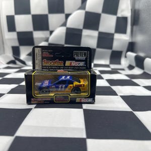 May include: A 1:64 scale die-cast replica of a NASCAR race car. The car is blue and yellow with the number 11 on the roof and sides. The car is in its original packaging, which includes the text "PREVIEW 1996 EDITION" and "LOWE'S".