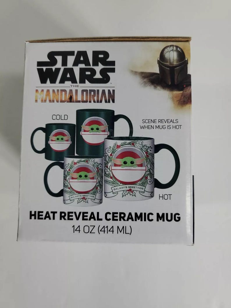 Pode incluir: Caneca de cer&acirc;mica Star Wars: The Mandalorian com revela&ccedil;&atilde;o de calor. A caneca apresenta um design com Grogu e o texto "Galaxy's Greetings". A caneca cont&eacute;m 414 ml de l&iacute;quido. O design muda com o calor.