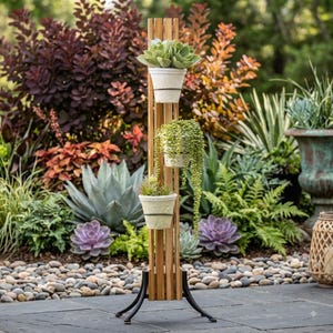 May include: A vertical wooden plant stand with a black metal base, featuring three stacked white pots. The top pot holds a succulent, the middle pot contains a trailing string of pearls plant, and the bottom pot holds a small green plant.
