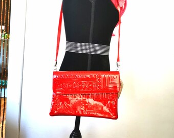 May include: A red patent leather crossbody bag with a geometric pattern. The bag has a flap closure and a silver chain strap.