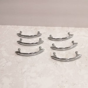 May include: Six silver-toned cabinet drawer pulls with a curved design. The pulls are arranged in two rows of three.