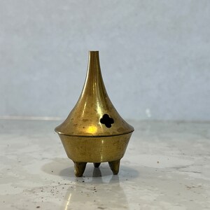 May include: A small, gold-coloured metal incense burner with three legs and a small hole in the top.