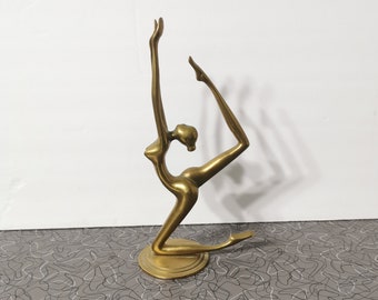 May include: A gold-toned metal sculpture of a person in a yoga pose. The sculpture is on a round base and is standing on a patterned surface.
