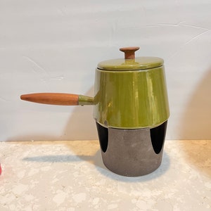 May include: A green enamel fondue pot with a wooden handle and lid. The pot sits on a black metal stand with two cutouts.