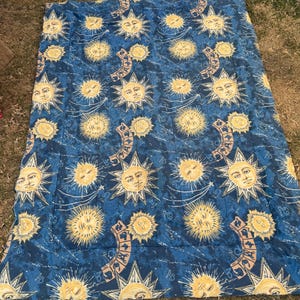 Peut inclure: Une couette bleue avec un motif répété de soleils jaunes et d'éléments célestes. La couette est rectangulaire et semble être faite d'un tissu doux. Les soleils ont des visages et sont entourés d'éclats d'étoiles.