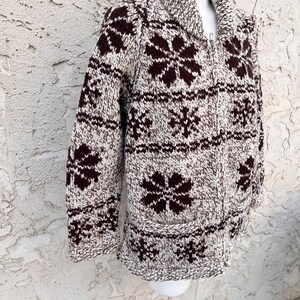 May include: A brown and white knitted cardigan with a snowflake pattern. The cardigan has a zipper closure and a collar.