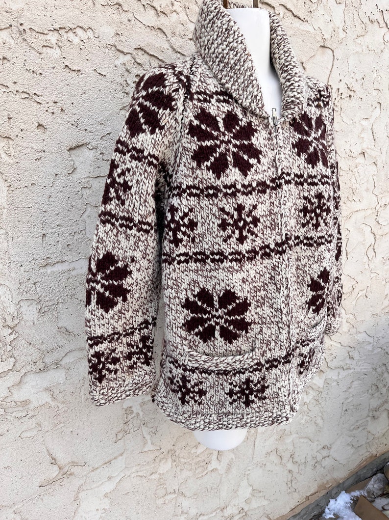 May include: A brown and white knitted cardigan with a snowflake pattern. The cardigan has a zipper closure and a collar.