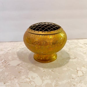 Puede incluir: Un quemador de incienso de metal dorado con un intrincado diseño floral y una parte superior de malla de alambre.