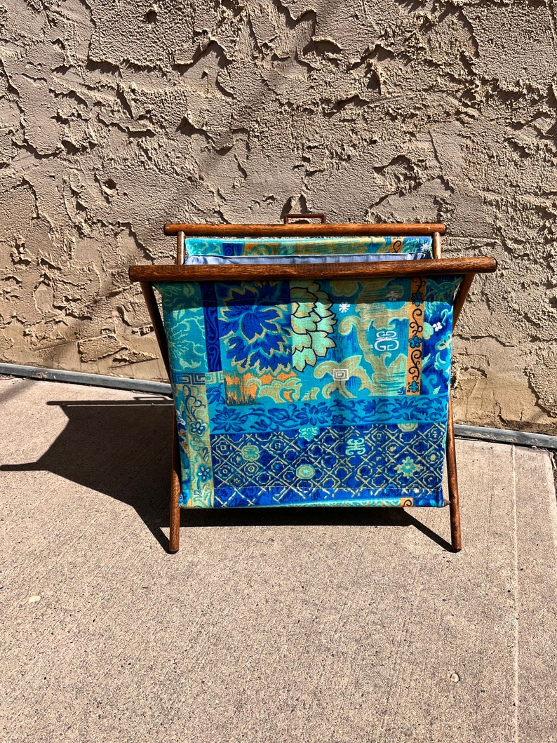 K&ouml;nnte beinhalten: Ein faltbarer Garnst&auml;nder aus Holz mit einer blauen und gr&uuml;nen gemusterten Stoffauskleidung. Der Stoff hat ein florales und geometrisches Muster.