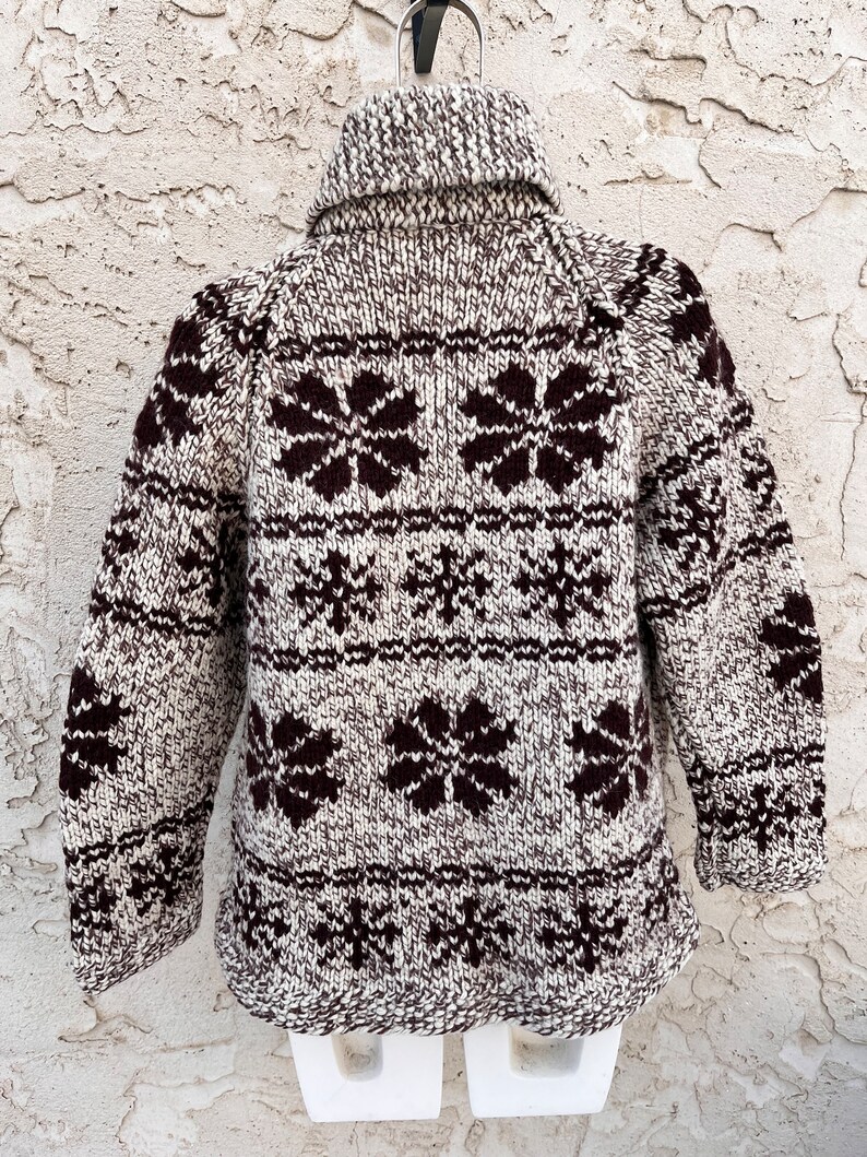 May include: A brown and white knit sweater with a snowflake and flower pattern. The sweater has a turtleneck collar and long sleeves.