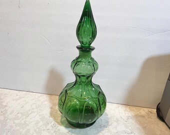 May include: A tall, green glass bottle with a textured, bulbous body and a pointed, ribbed stopper. The bottle has a vintage look and is perfect for displaying on a shelf or table.