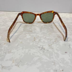May include: Sunglasses with a tortoiseshell frame and green lenses. The frame has a brown and yellow pattern. The sunglasses are open, with the arms extended. The lenses are a dark green color.