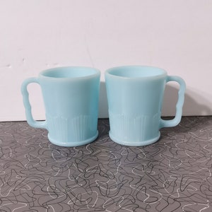 May include: Two light blue glass mugs with a fluted design. The mugs have a rounded shape and a handle on the side.