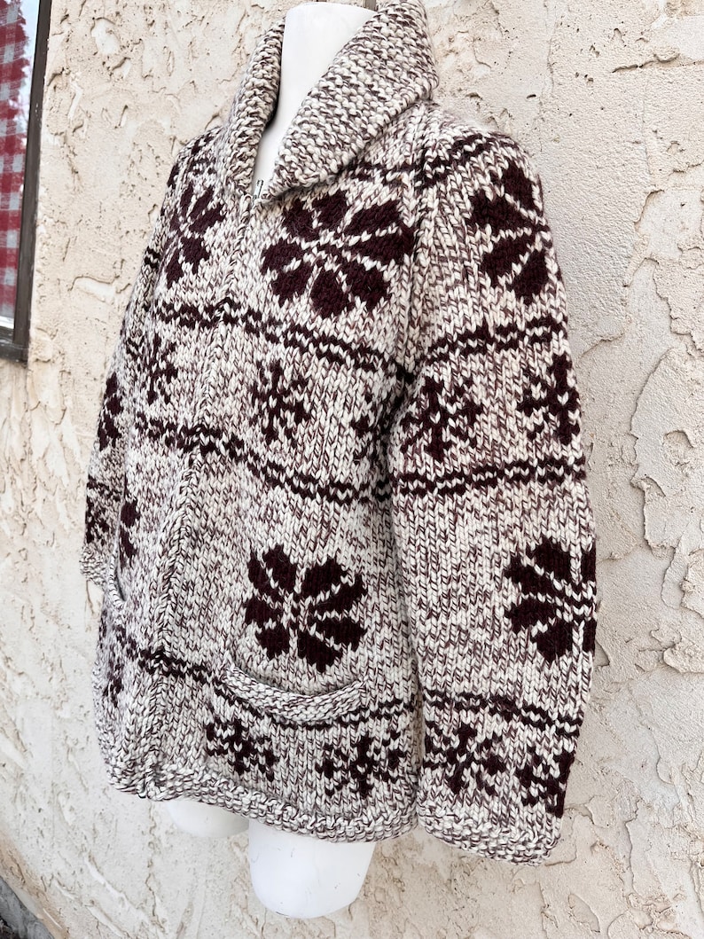 May include: A brown and white knit cardigan with a brown snowflake pattern. The cardigan has a shawl collar and a zipper closure.