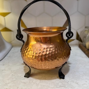 Peut inclure: Un chaudron en cuivre avec une texture martelée et une poignée en métal noir. Le chaudron a trois pieds décoratifs. Le cuivre a une surface brillante et réfléchissante. Conçu pour un usage décoratif ou fonctionnel.