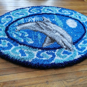 May include: A blue and white round rug with a dolphin design. The rug is made of a fluffy, textured material.