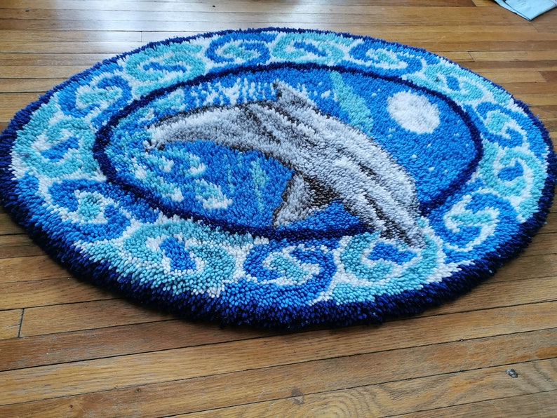 May include: A blue and white round rug with a dolphin design. The rug is made of a fluffy, textured material.