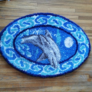 May include: A blue and white oval rug with a design of two dolphins jumping out of the water. The rug has a white border with a blue and white pattern.