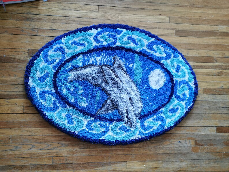 May include: A blue and white oval rug with a design of two dolphins jumping out of the water. The rug has a white border with a blue and white pattern.