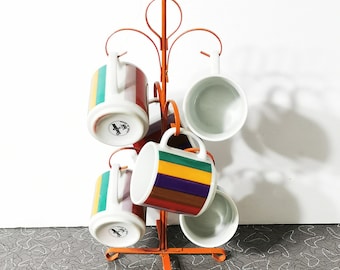 May include: Orange metal mug tree with six white mugs. The mugs have colorful stripes and some have the word "Caffe" printed on them.
