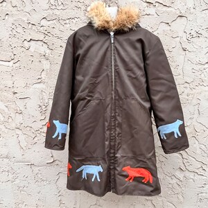 May include: A brown long-sleeved jacket with a faux fur hood. The jacket has a zip fastening and features blue and orange animal silhouettes on the sleeves and hem.